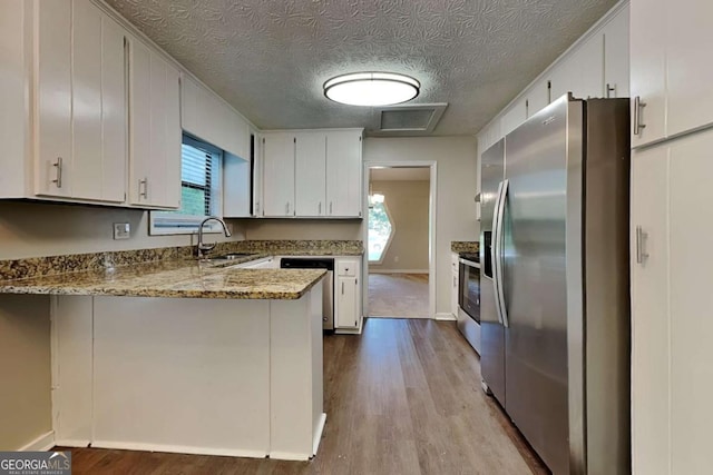 kitchen with stainless steel appliances, kitchen peninsula, light stone countertops, sink, and white cabinetry