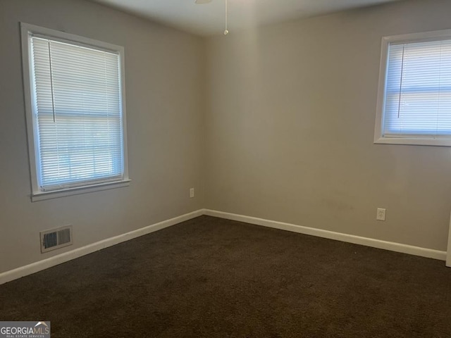 unfurnished room featuring ceiling fan, plenty of natural light, and dark colored carpet