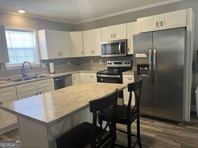 kitchen with a breakfast bar area, appliances with stainless steel finishes, ornamental molding, sink, and white cabinetry