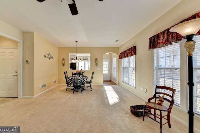 dining room with light colored carpet and ceiling fan with notable chandelier