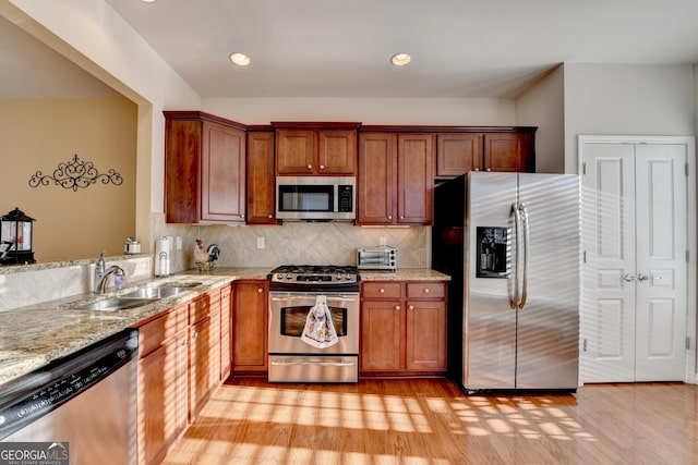 kitchen with light stone countertops, light hardwood / wood-style flooring, backsplash, appliances with stainless steel finishes, and sink