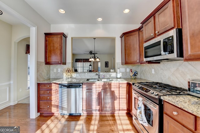 kitchen with stainless steel appliances, sink, light stone counters, ceiling fan, and light hardwood / wood-style flooring