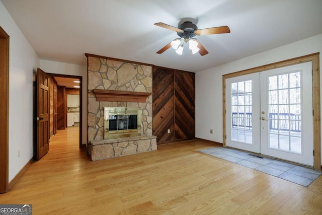 unfurnished living room with light wood-type flooring, ceiling fan, french doors, wooden walls, and a fireplace