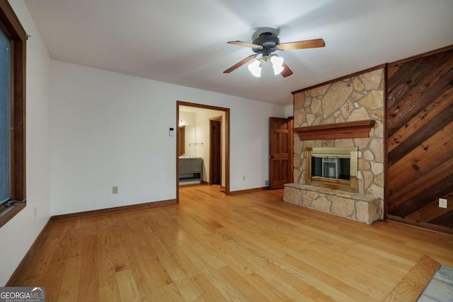 unfurnished living room with light hardwood / wood-style floors, ceiling fan, wood walls, and a fireplace