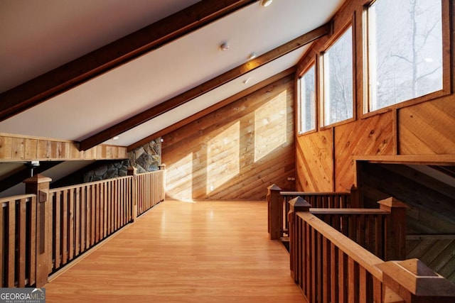 interior space with light wood-type flooring, wooden walls, and vaulted ceiling with beams