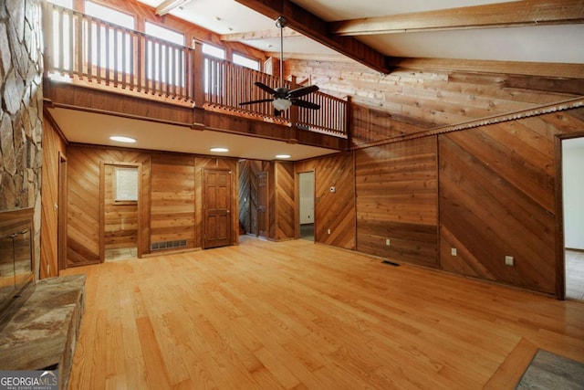 unfurnished living room with beam ceiling, ceiling fan, light hardwood / wood-style floors, and wood walls