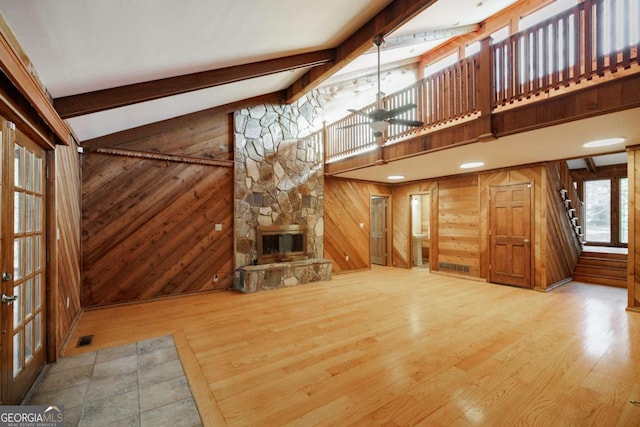 unfurnished living room with a stone fireplace, lofted ceiling with beams, wood walls, and wood-type flooring