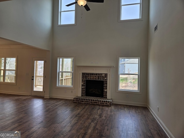 unfurnished living room featuring visible vents, a fireplace, baseboards, ceiling fan, and dark wood-style flooring