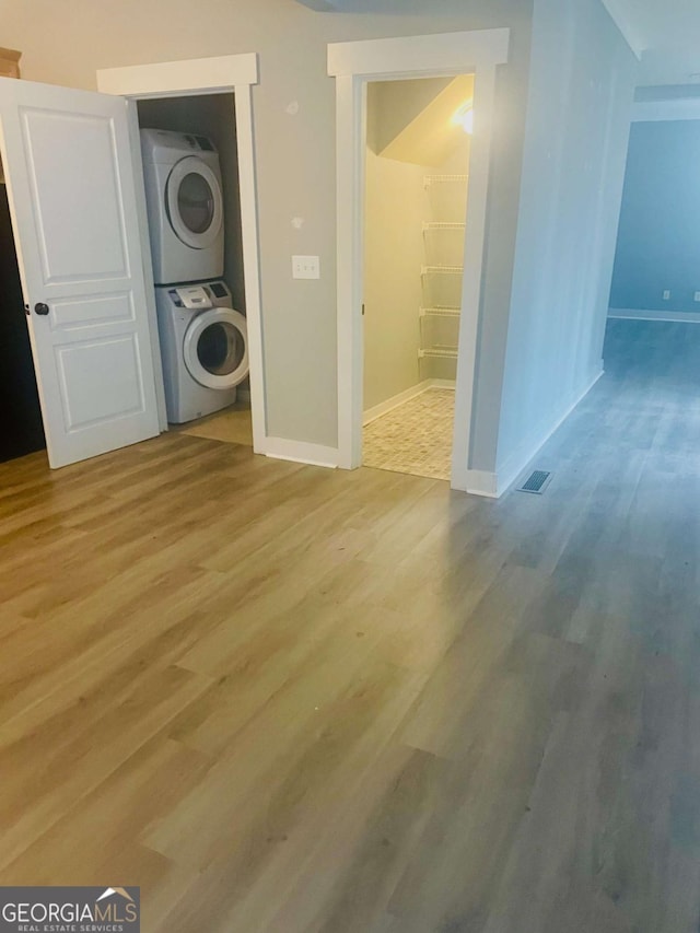 clothes washing area with stacked washer / drying machine and light wood-type flooring