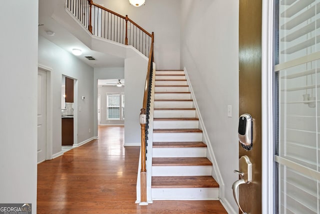 stairway with a towering ceiling, hardwood / wood-style floors, and ceiling fan