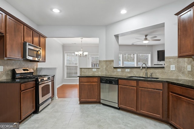 kitchen featuring sink, appliances with stainless steel finishes, kitchen peninsula, ceiling fan with notable chandelier, and dark stone counters