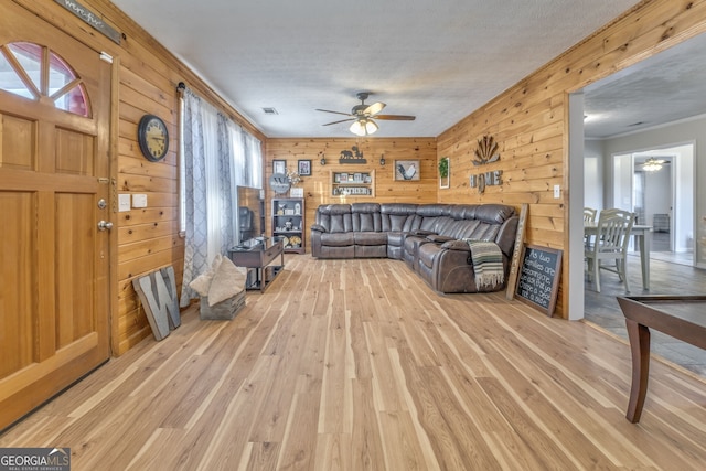 living room featuring wooden walls, a textured ceiling, ceiling fan, light hardwood / wood-style flooring, and crown molding