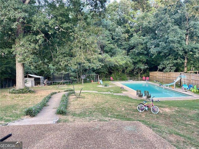 view of swimming pool featuring a lawn, a trampoline, and a water slide