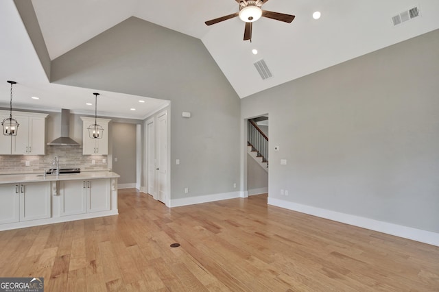 kitchen with white cabinets, ceiling fan, decorative backsplash, wall chimney range hood, and pendant lighting