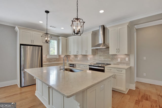 kitchen featuring stainless steel appliances, an island with sink, wall chimney range hood, white cabinetry, and sink