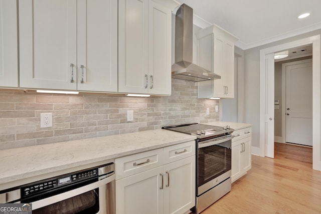 kitchen with white cabinetry, light stone counters, wall chimney exhaust hood, electric range, and crown molding