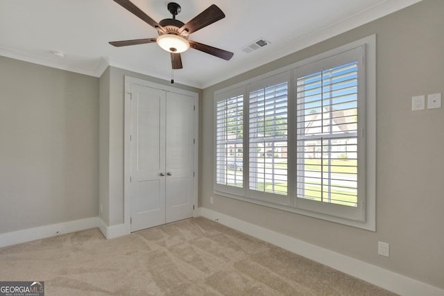 unfurnished bedroom featuring a closet, ceiling fan, crown molding, and light colored carpet