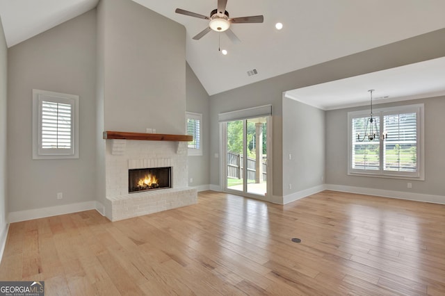 unfurnished living room featuring ceiling fan with notable chandelier, high vaulted ceiling, a brick fireplace, and light hardwood / wood-style floors