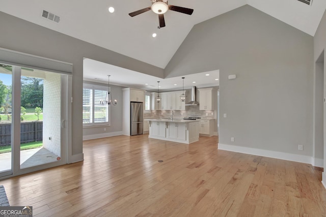 unfurnished living room featuring ceiling fan with notable chandelier, high vaulted ceiling, and light wood-type flooring