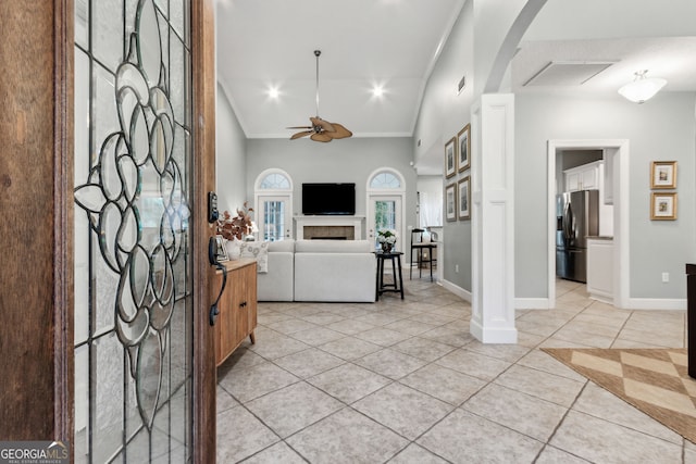 entryway featuring a tiled fireplace, light tile patterned floors, ceiling fan, ornamental molding, and high vaulted ceiling