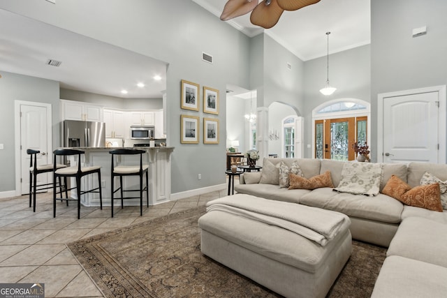 living room with a high ceiling, ceiling fan, light tile patterned floors, and crown molding