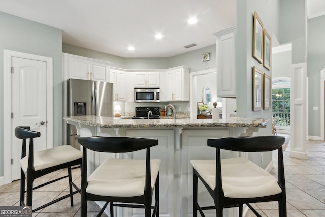 kitchen featuring appliances with stainless steel finishes, a kitchen bar, light stone counters, white cabinets, and light tile patterned flooring