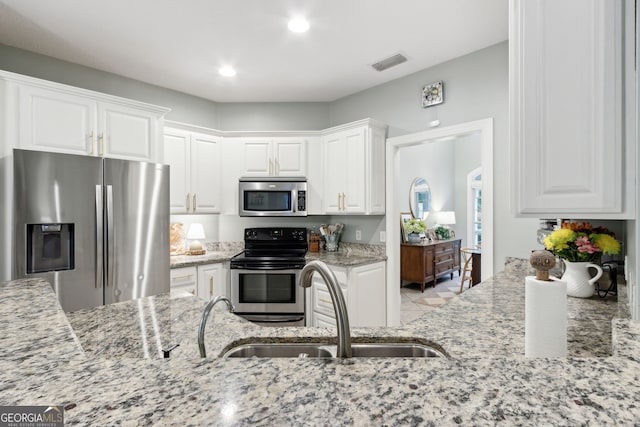 kitchen featuring light stone counters, stainless steel appliances, white cabinets, and sink