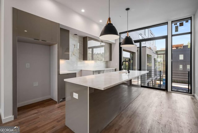 kitchen with decorative light fixtures, a center island with sink, a wall of windows, and dark hardwood / wood-style flooring