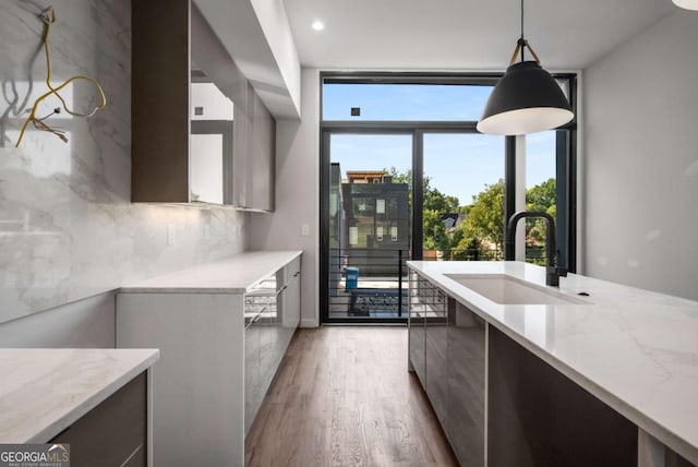 kitchen featuring hanging light fixtures, light wood-type flooring, light stone countertops, sink, and backsplash