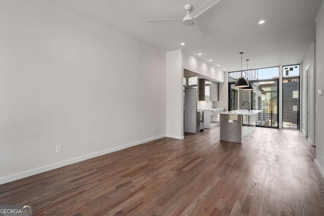 unfurnished living room with sink, ceiling fan, a wall of windows, and dark hardwood / wood-style floors