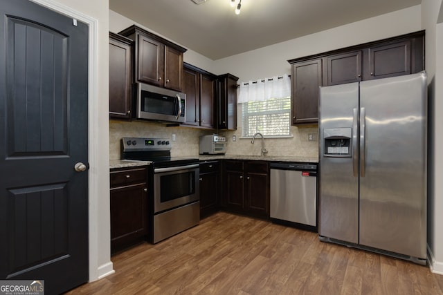 kitchen with appliances with stainless steel finishes, dark brown cabinets, backsplash, and hardwood / wood-style flooring