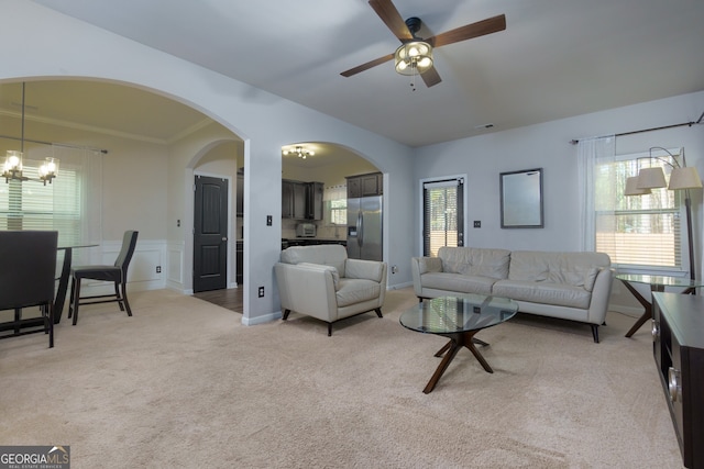 carpeted living room with ceiling fan with notable chandelier