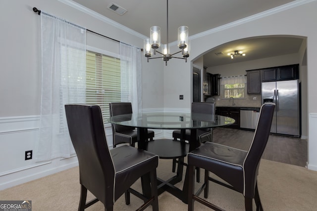 dining area with sink, a chandelier, crown molding, and carpet flooring