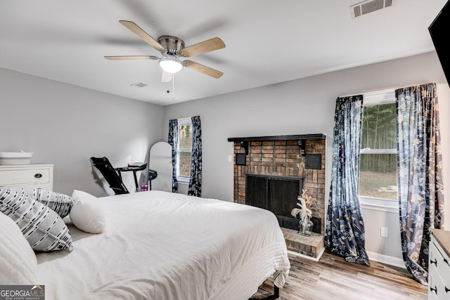 bedroom featuring ceiling fan, light wood-type flooring, and a brick fireplace