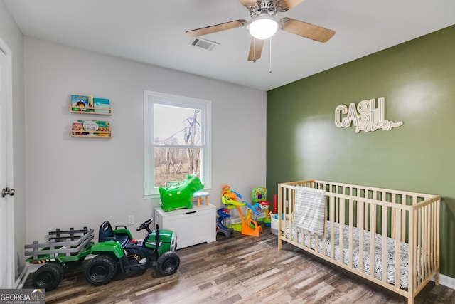 bedroom with a crib, wood-type flooring, and ceiling fan