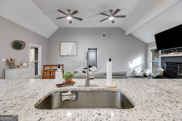 kitchen featuring sink, lofted ceiling, ceiling fan, and light stone counters