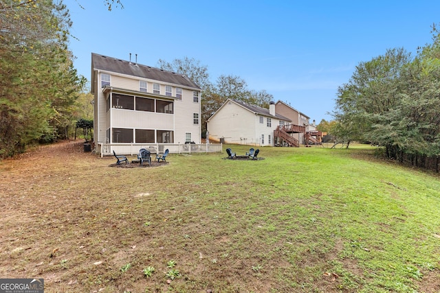 back of property featuring a sunroom, a yard, a fire pit, and a wooden deck