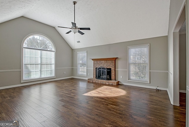 unfurnished living room with a textured ceiling, vaulted ceiling, dark hardwood / wood-style floors, a fireplace, and ceiling fan