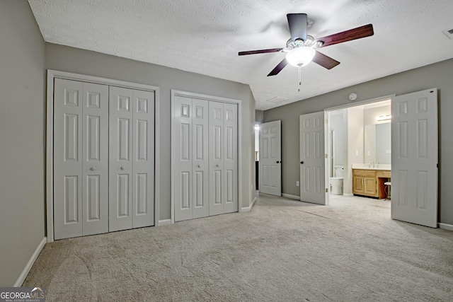 unfurnished bedroom with light colored carpet, connected bathroom, ceiling fan, and multiple closets