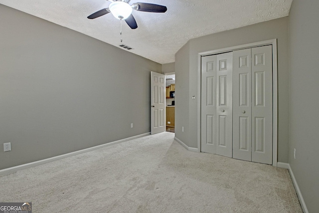 unfurnished bedroom with a textured ceiling, ceiling fan, a closet, and light carpet