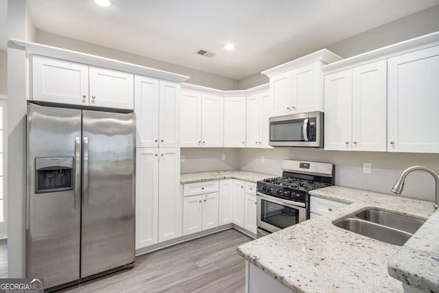 kitchen with stainless steel appliances, white cabinetry, sink, and light stone counters