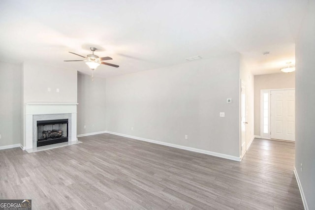 unfurnished living room featuring a high end fireplace, ceiling fan, and wood-type flooring