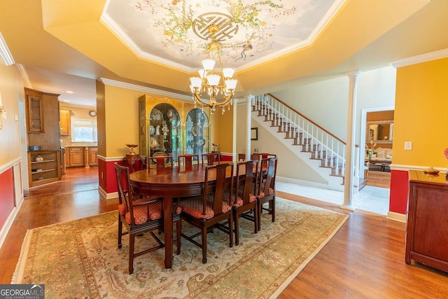 dining space featuring wood-type flooring, a raised ceiling, a notable chandelier, and crown molding