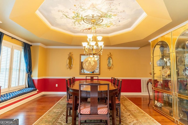 dining area with a raised ceiling, a notable chandelier, crown molding, and wood-type flooring