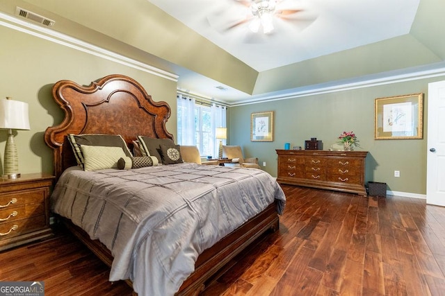 bedroom with dark wood-type flooring, ceiling fan, and a tray ceiling