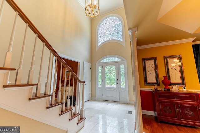 foyer entrance featuring a towering ceiling, an inviting chandelier, crown molding, and ornate columns