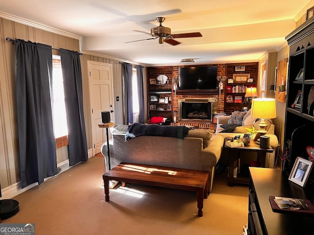 carpeted living room featuring built in shelves, wood walls, ornamental molding, ceiling fan, and a fireplace