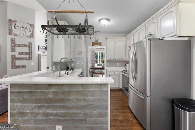 kitchen featuring kitchen peninsula, a textured ceiling, stainless steel appliances, backsplash, and white cabinetry