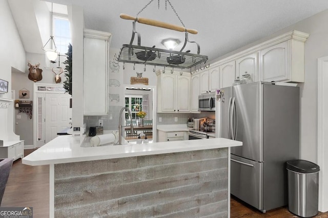 kitchen with kitchen peninsula, stainless steel appliances, backsplash, dark hardwood / wood-style flooring, and white cabinetry