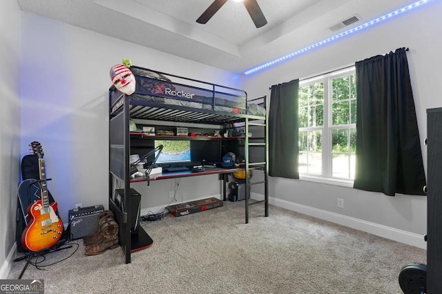 carpeted bedroom with ceiling fan and a tray ceiling